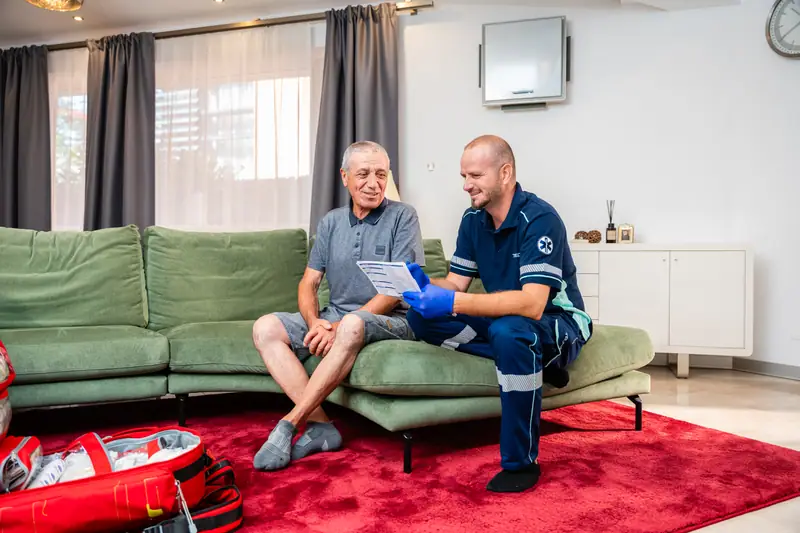 Asistent medical TRUMED lângă un pacient vârstnic, în camera de zi