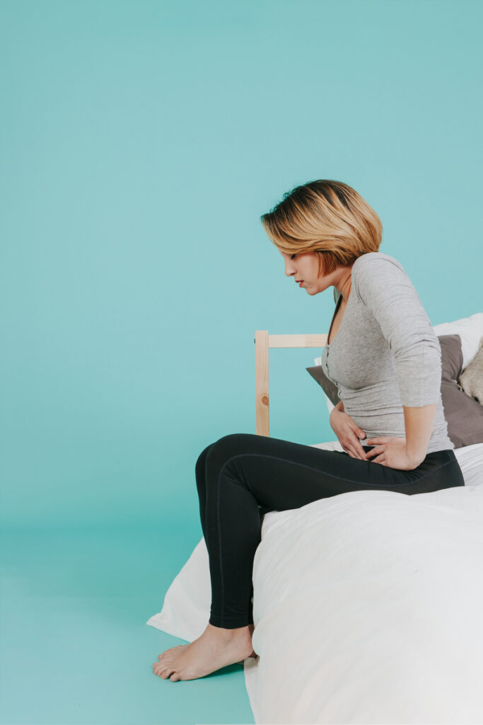 3.2. Ce poți face acasă – dar cu recomandarea specialistului – pentru a trata retenția urinara - femeie care sta pe pat cu dureri de abdomen